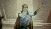 a woman in a blue costume is standing in front of a gma logo .