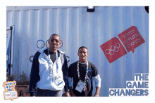 two men stand in front of a youth olympic games sign