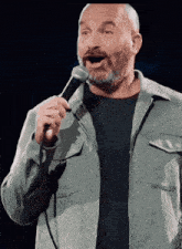 a man with a beard is singing into a microphone while wearing a grey jacket