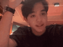 a young man wearing a black shirt and a watch looks at the camera