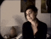 a woman in a black shirt is sitting in a room with a lamp .
