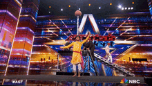 a man stands on a stage holding a basketball in front of a nbc logo