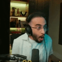 a man wearing headphones and glasses is sitting in front of a microphone in a room .