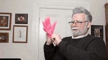 a man wearing glasses and a black sweater is holding up a pink glove