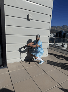 a man in a hospital gown squatting with a cane in front of a building