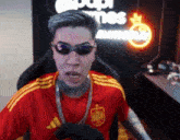 a man wearing sunglasses and a red adidas shirt is sitting in a chair