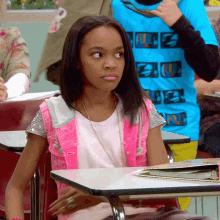 a girl in a pink vest is sitting at a desk