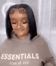 a woman is wearing a hoodie with the word essentials on it .