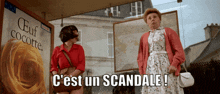 two women are standing in front of a sign that says " c'est un scandale "
