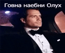 a man in a tuxedo and bow tie is sitting in the back seat of a car at night .