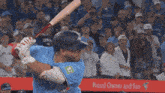 a baseball player swings at a pitch in front of a proud owner and fan banner