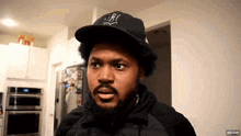 a man with a beard is wearing a black hat with the letter t on it