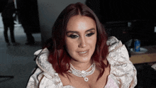 a woman with red hair is wearing a white dress and a pearl necklace