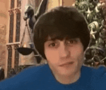 a young man with a blue shirt on is standing in front of a christmas tree .