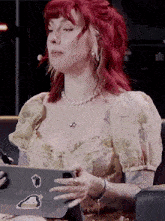 a woman with red hair is sitting in front of a microphone holding a laptop and a cell phone .