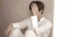 a man in a white shirt is covering his face with his hand .
