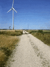 a dirt road with a large wind turbine in the background