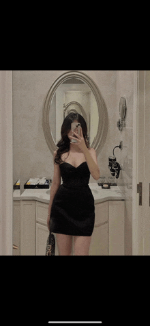 a woman in a black dress is taking a picture of herself in a mirror