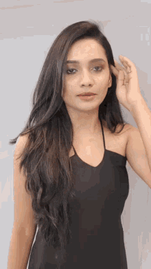 a woman with long hair is wearing a black dress and touching her hair