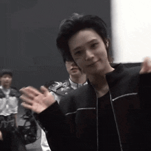 a man in a black jacket is waving his hands in front of a group of people .