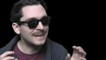 a man wearing sunglasses and a sweater is making a funny face in a dark room .