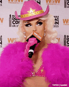 a woman in a pink cowboy hat is holding a microphone in front of a wall that says wow