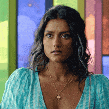 a woman wearing a blue top and a gold necklace is looking at the camera