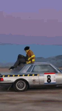 a man in a fireman 's uniform is sitting on top of a silver car with the number 8 on it .