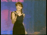 a woman in a black dress singing into a microphone on a stage