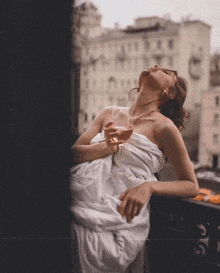 a woman in a white dress is sitting on a balcony with a glass of wine