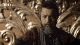 a man with a beard is sitting on a throne with trt1 written on the bottom right