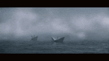 two paper boats are floating in the ocean in the fog .