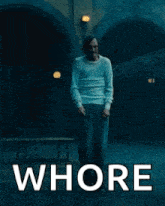 a man in a white shirt is standing in front of a building with the words `` whore '' written on the poster .