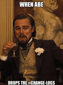 a man in a suit holds a glass of wine and says when abe drops the change-logs