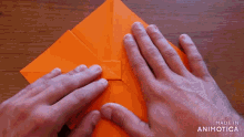 a person is folding an orange piece of paper with the words made in animotica visible