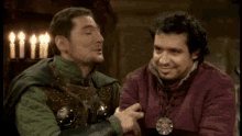 a man in a knight 's armor is talking to another man in a dark room .