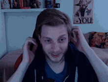 a man adjusts his ear buds in front of a poster that says you