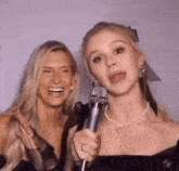 two women are standing next to each other and one is holding a microphone .