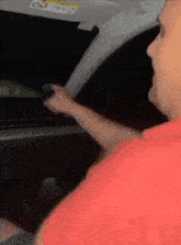 a man in a red shirt is driving a car and holding a steering wheel .