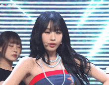 a woman wearing a pearl necklace stands in front of a striped background