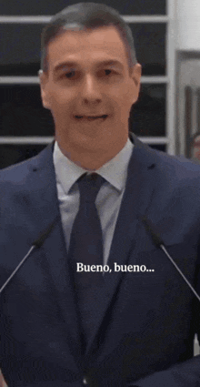 a man in a suit and tie is speaking into a microphone and the words bueno bueno are visible