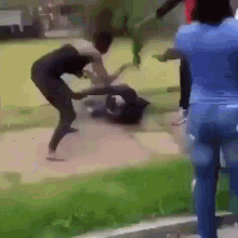 a group of people are fighting on a sidewalk while a woman watches .