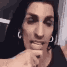 a woman wearing hoop earrings is making a funny face while holding her hand to her mouth .
