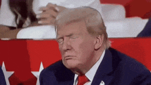 donald trump is sitting in a stadium with his eyes closed and making a funny face .