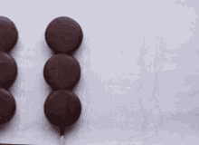 three chocolate covered cookies on sticks on a white background