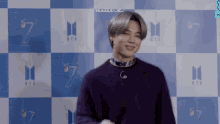 a man wearing a purple sweater and a scarf is standing in front of a blue checkered wall .