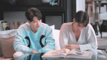 two men are sitting at a table reading a book .