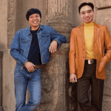 two men standing next to each other one wearing a denim jacket and the other wearing an orange jacket