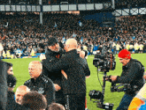 a man in a black nike jacket is hugging another man on the field