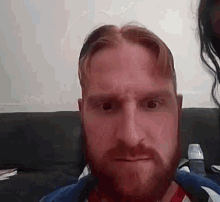 a man with a beard is sitting on a couch and making a funny face .
